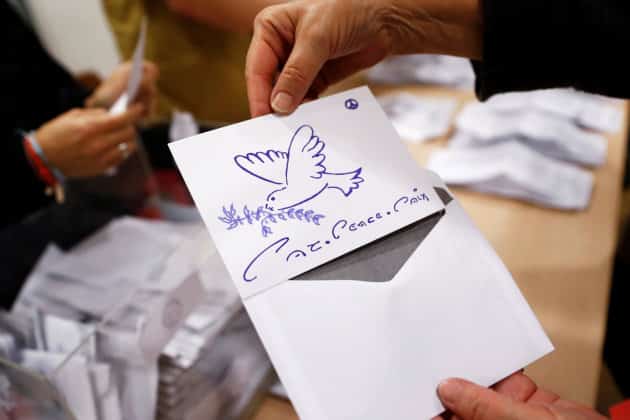 Un miembro de la mesa electoral muestra un voto nulo con el dibujo de una paloma y el lema "paz" en varios idiomas